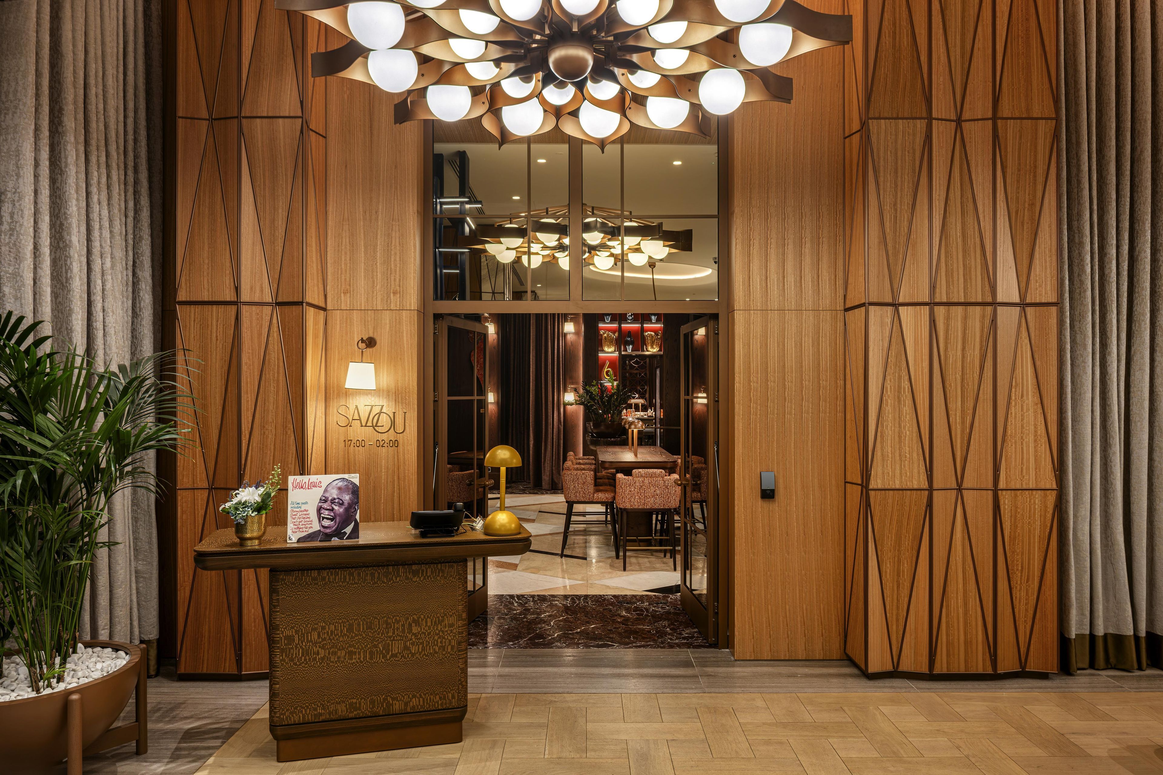 Um saguão de hotel com uma mesa de recepção, um lustre grande e vista para a área de refeições.