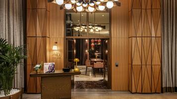 Um saguão de hotel com uma mesa de recepção, um lustre grande e vista para a área de refeições.