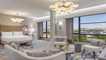 A modern hotel room with a large bed, two sofas, a coffee table, and a view of a cityscape through large windows.