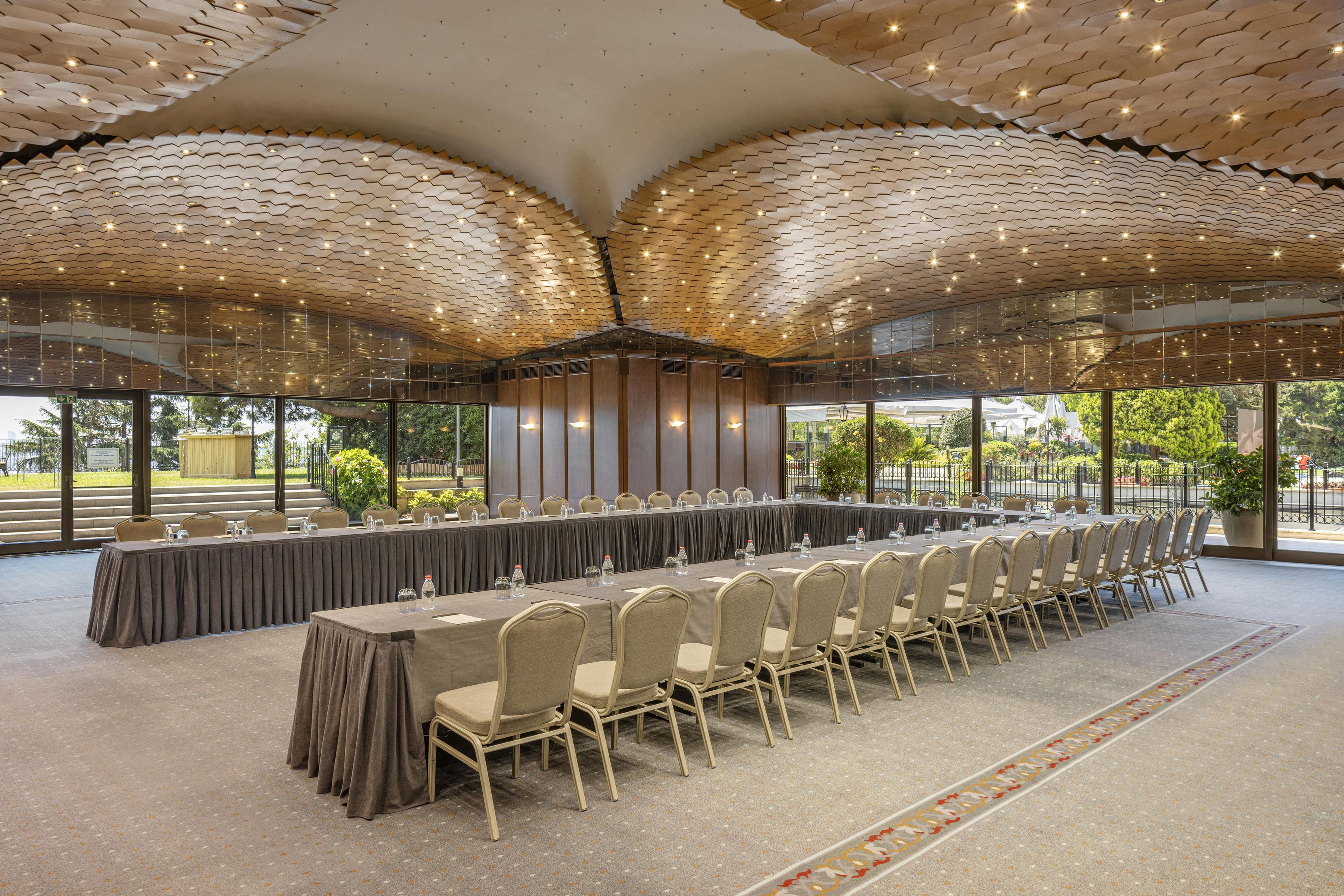 A conference room with a long table and chairs, large windows, and a unique ceiling design.