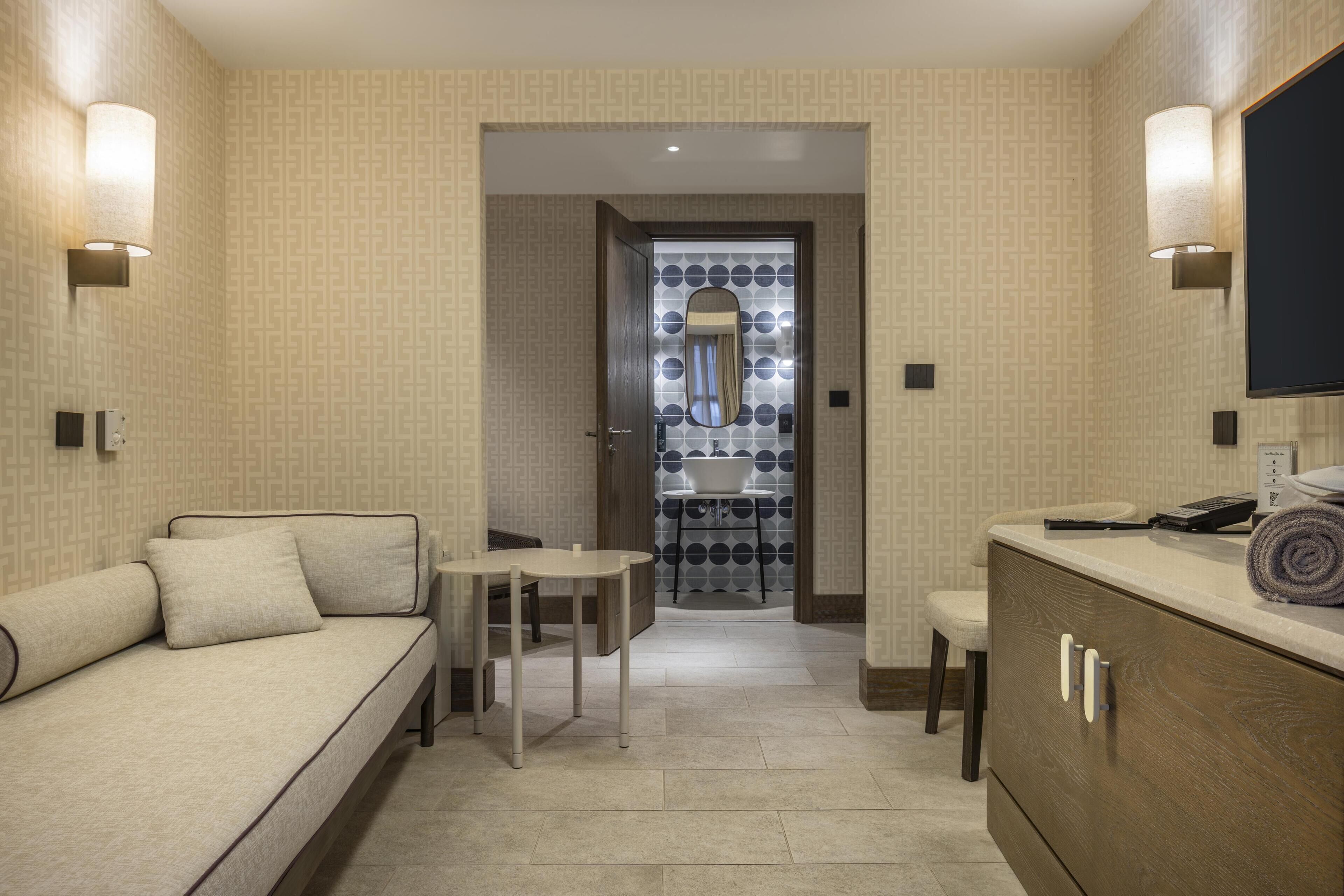 A hotel room with a sofa, a small table, a cabinet, and a mirror.
