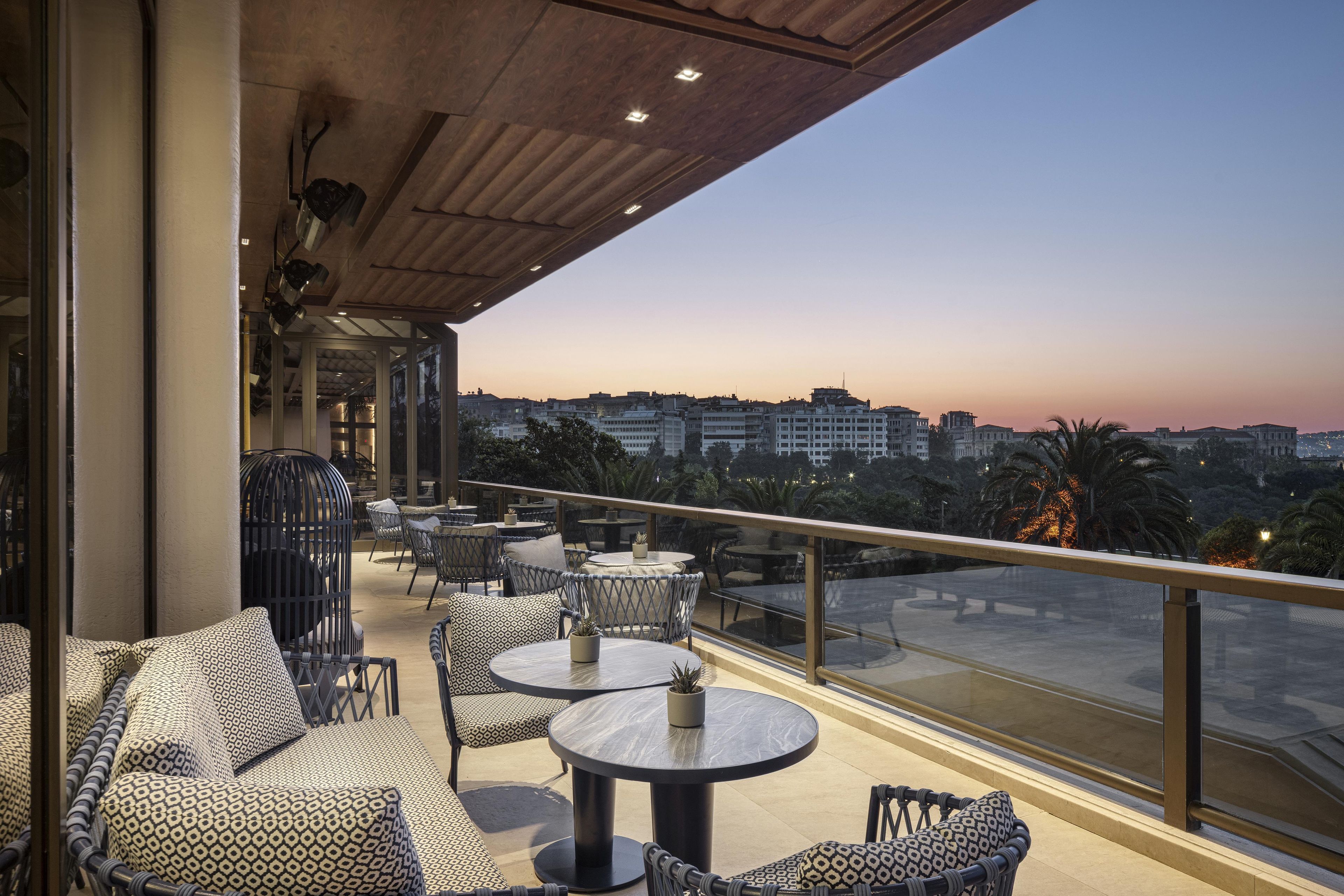 A rooftop terrace with outdoor seating, a view of the cityscape, and a clear sky.