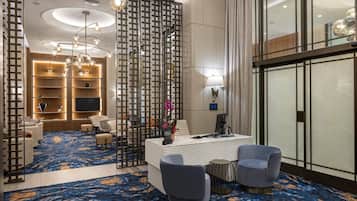 Un hall d’hôtel moderne avec un tapis à motifs bleus, un comptoir d’accueil, un espace salon et un mur décoratif orné d’un motif géométrique.