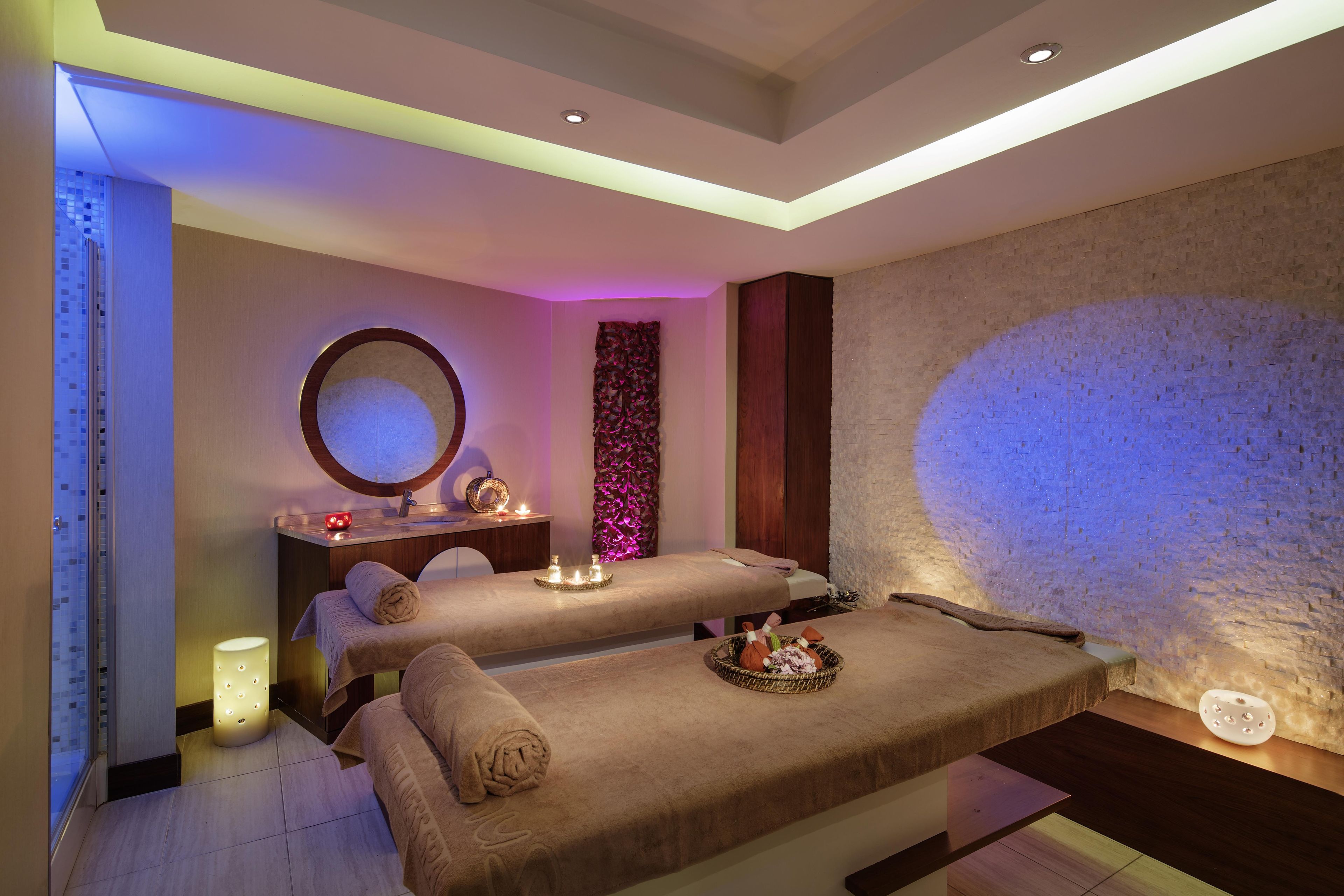 Een spa-ruimte met twee massagetafels, een spiegel, een wandverwarming en een decoratief paneel.
