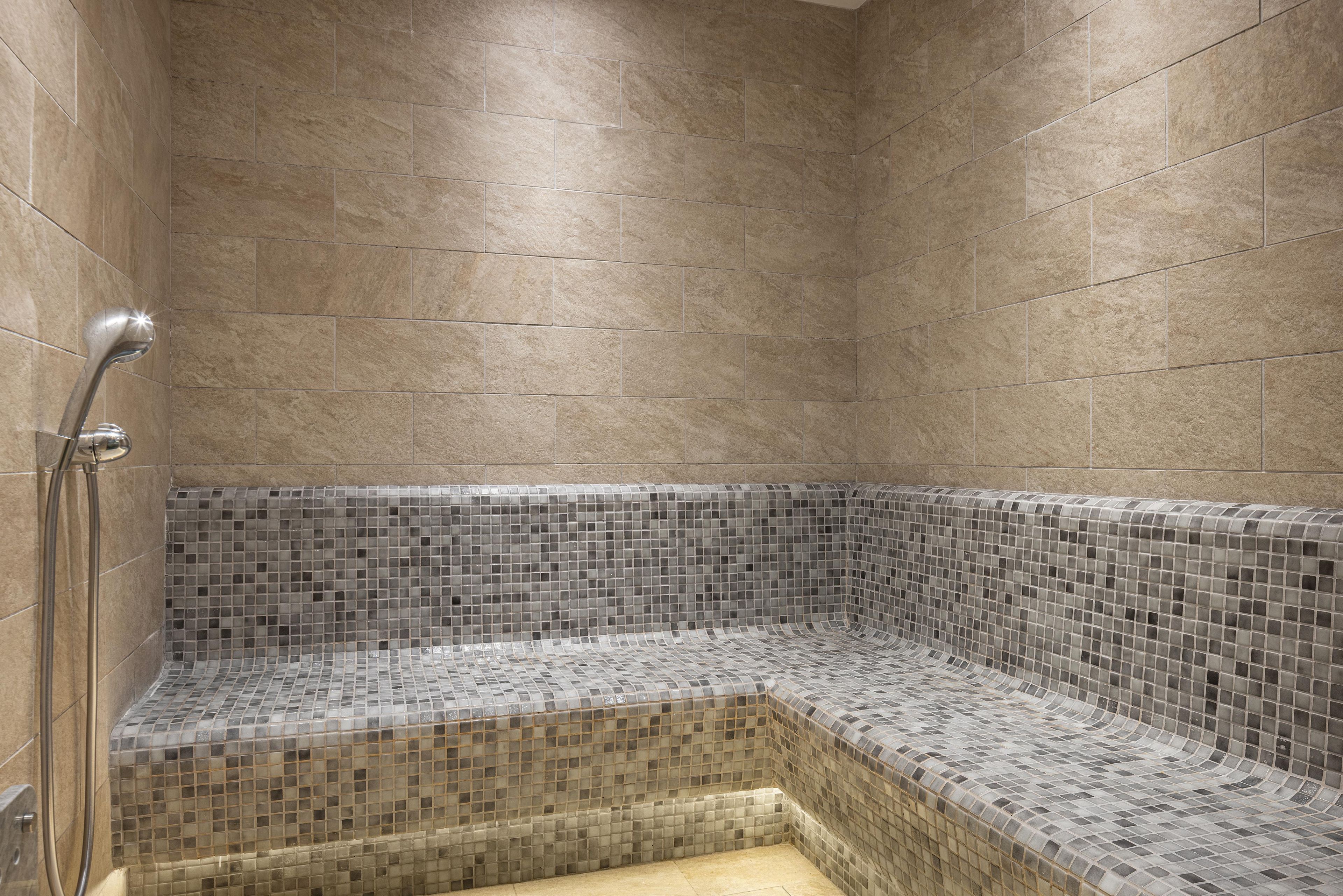 Un espace douche avec des murs carrelés et un banc en mosaïque de verre.