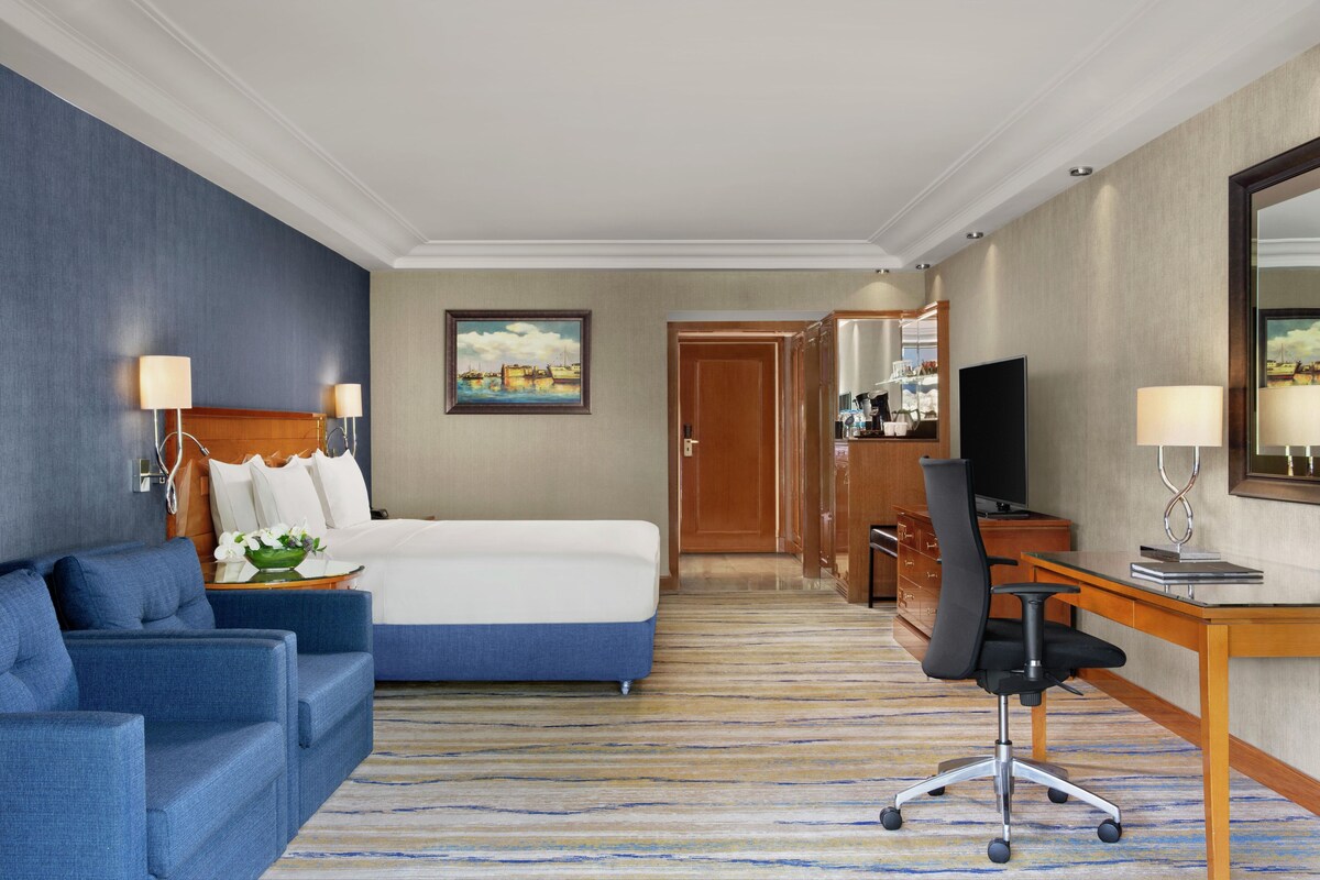 Una habitación de hotel con cama, sofá azul, escritorio y televisión.