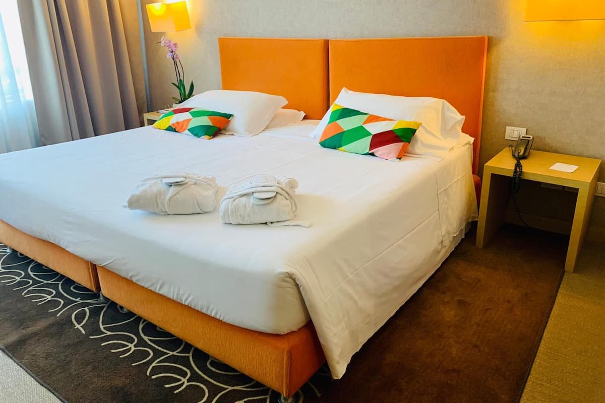 A hotel room with a large bed, two pillows, a bedside table with a phone, and a lamp.