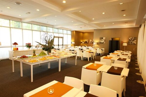A hotel conference room with white tables and chairs, a buffet table with fruits and vegetables, and large windows providing natural light. - Hotel Blaise & Francis (Milan)