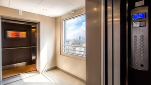 An elevator with a digital display, a window with a city view, and a door with a framed artwork. - Hotel Blaise & Francis (Milan)