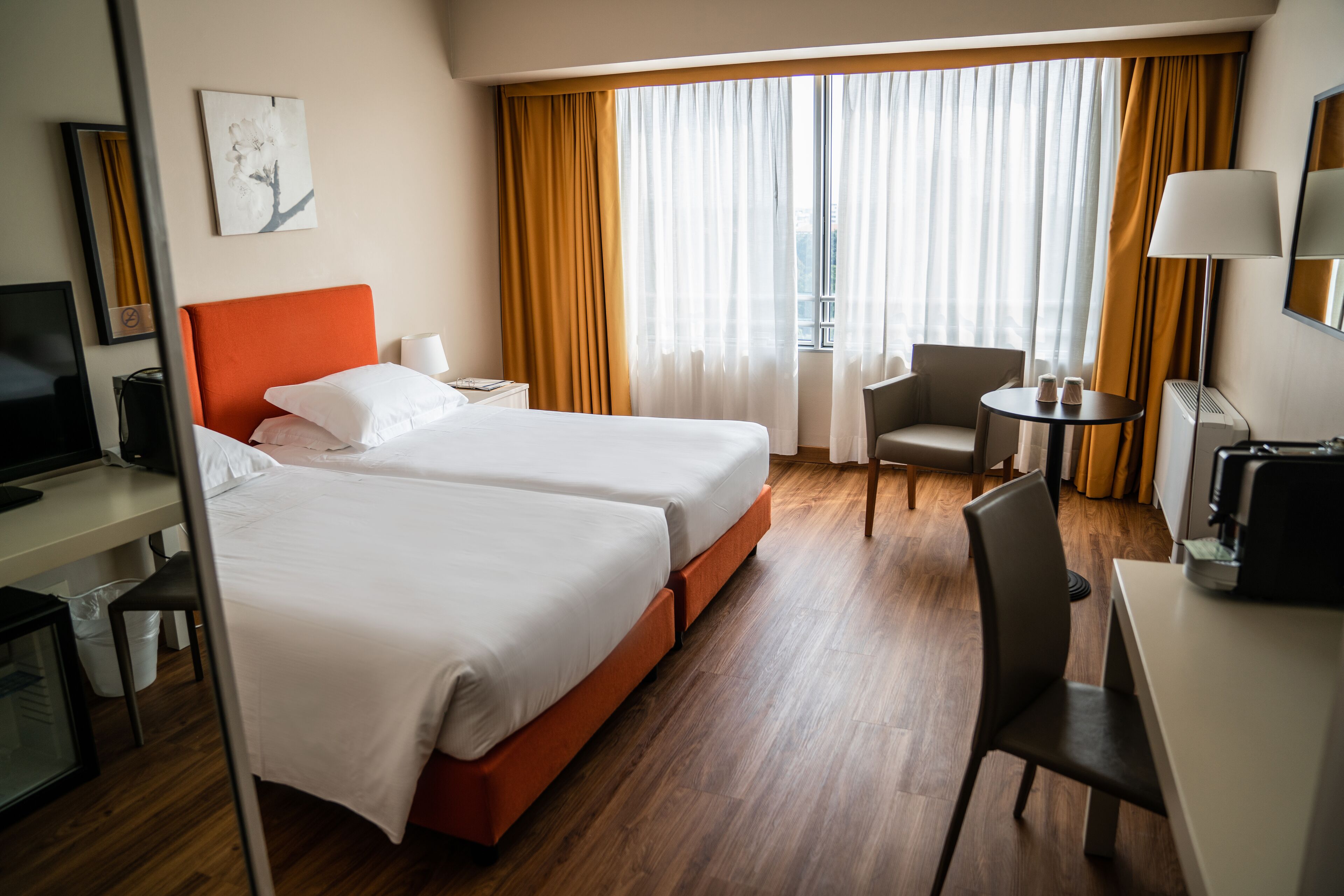 Une chambre d’hôtel avec deux lits, un bureau, une chaise, une petite table et un téléviseur.