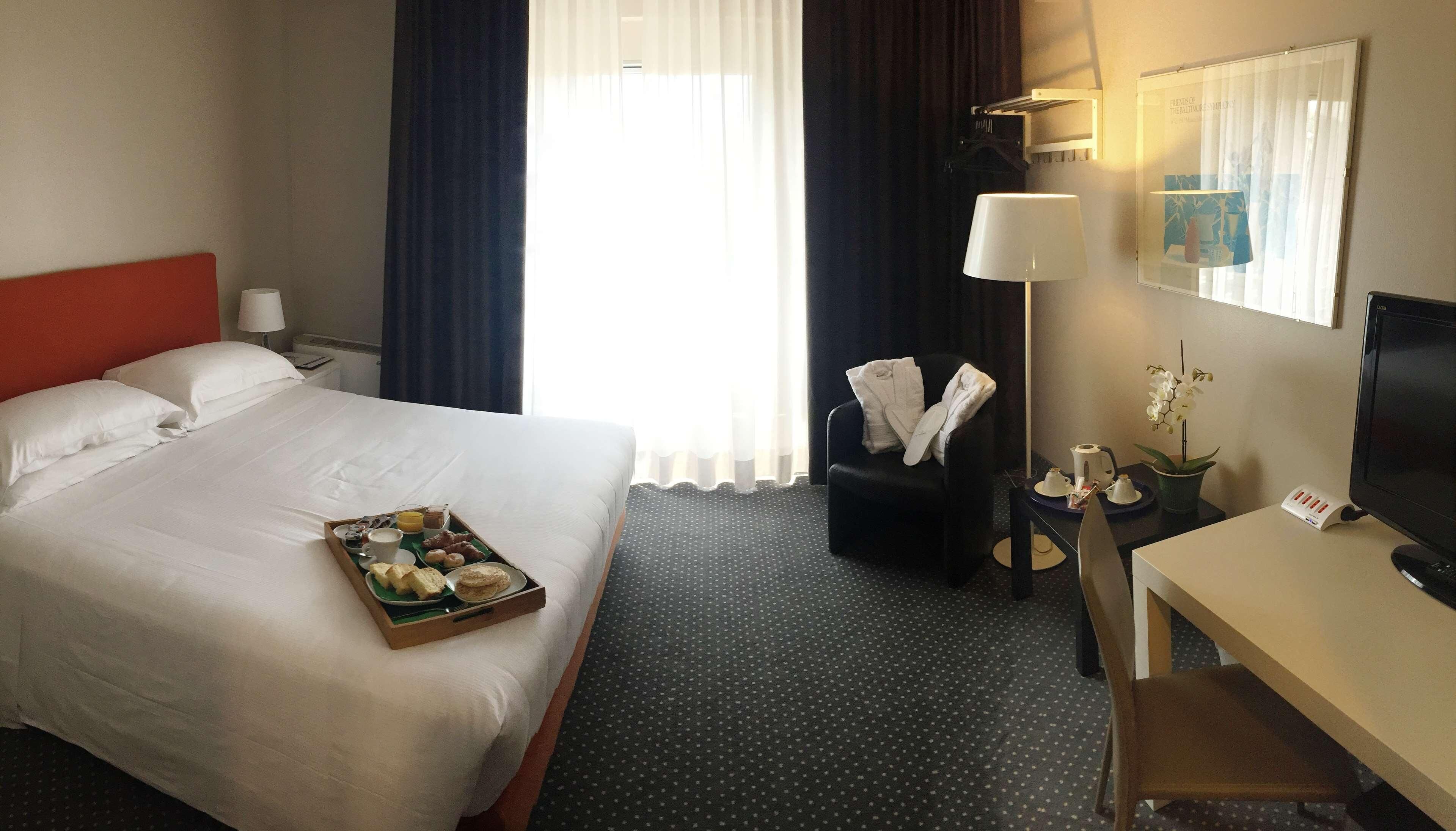 A hotel room with a bed, a desk, a chair, a TV, and a window with curtains.