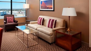 Une chambre d’hôtel avec un canapé, un fauteuil et une table. Une grande fenêtre offre une vue sur la ville.