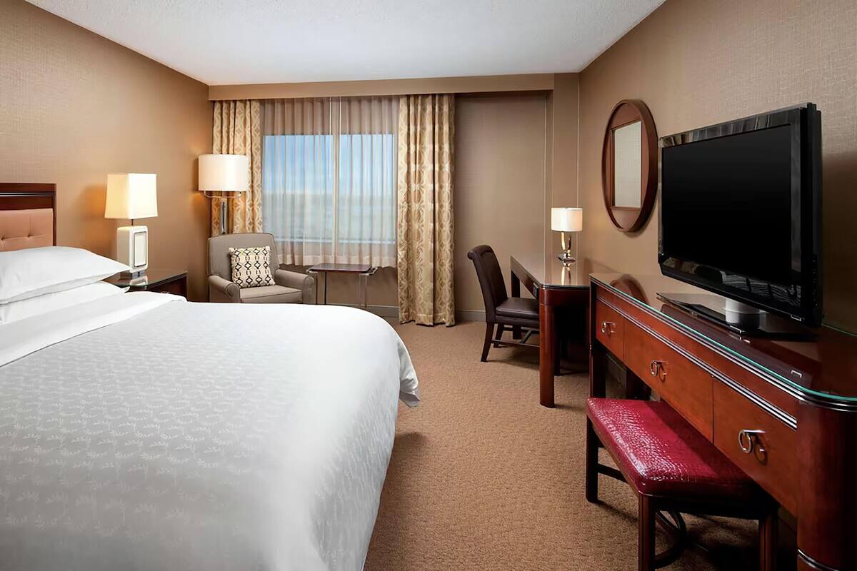 Une chambre d’hôtel avec un grand lit, un bureau avec une télévision, une chaise, une petite table et une fenêtre avec des rideaux.