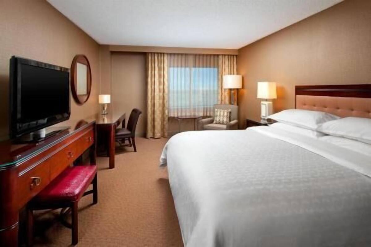 Een hotelkamer met een bed, een televisie, een bureau met een stoel, een lamp en een raam met gordijnen.