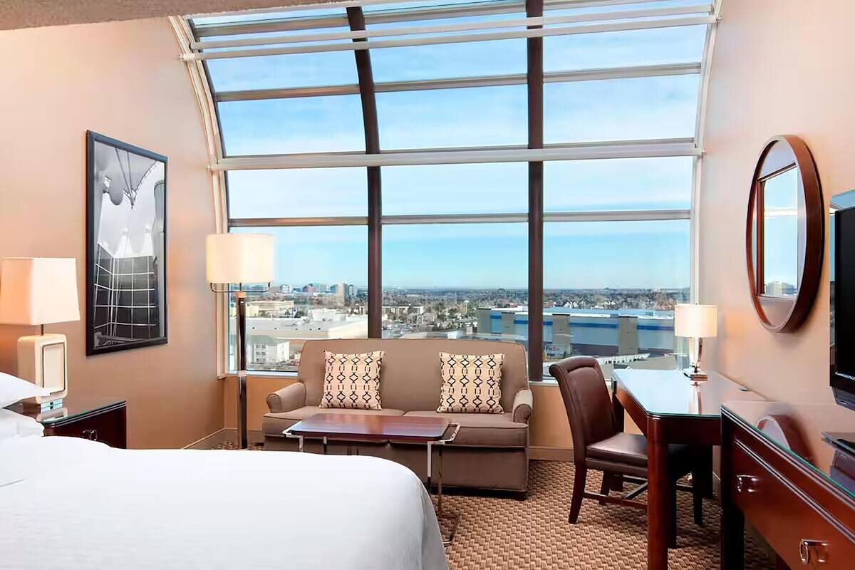 Une chambre d’hôtel comprenant un lit, un canapé, un bureau, une chaise, une télévision, une lampe et une grande fenêtre donnant sur la ville.