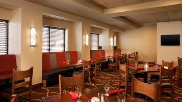 A hotel dining area with booths and tables, red and black seating, and a carpeted floor.