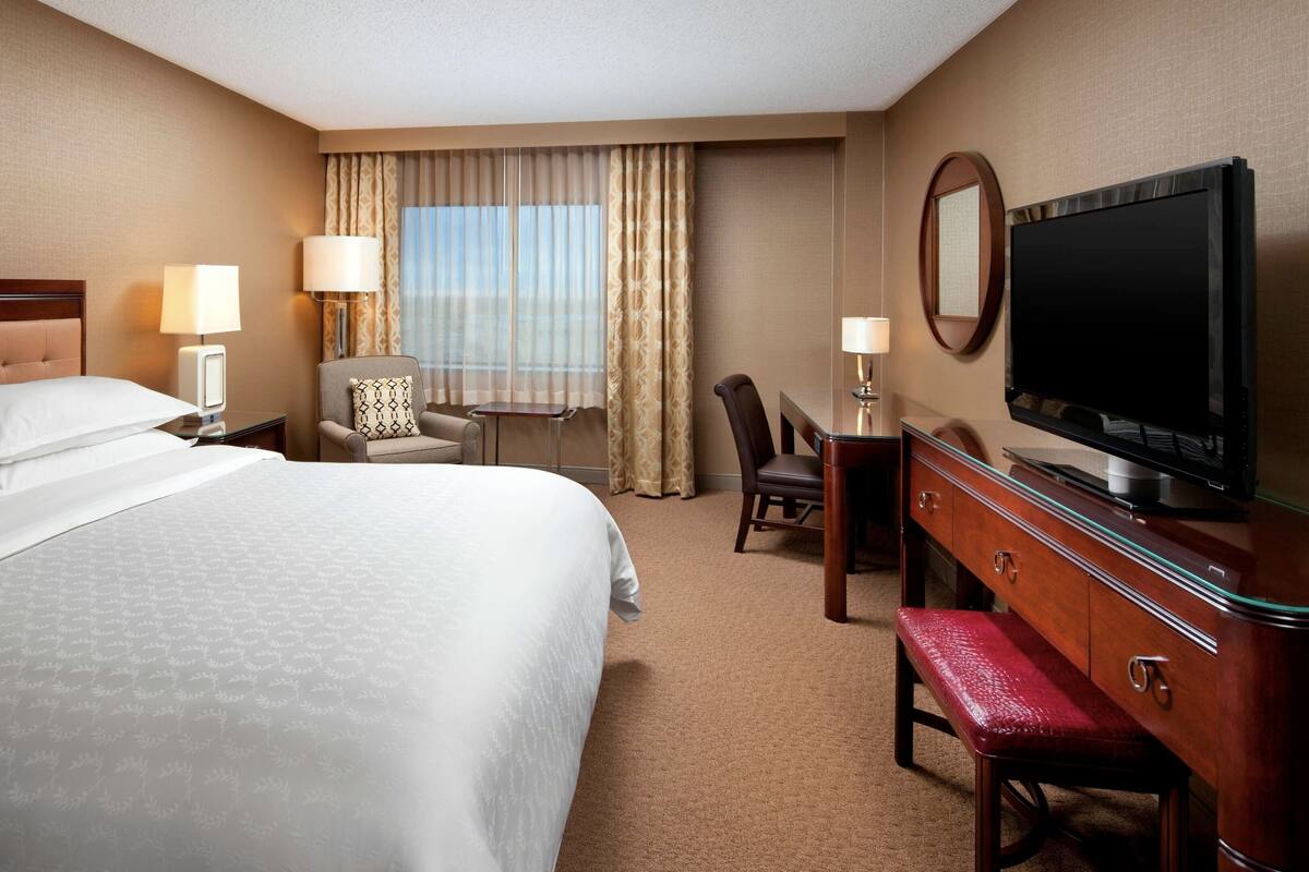 Une chambre d’hôtel avec un grand lit, un bureau avec une télévision, une chaise et une lampe de bureau.