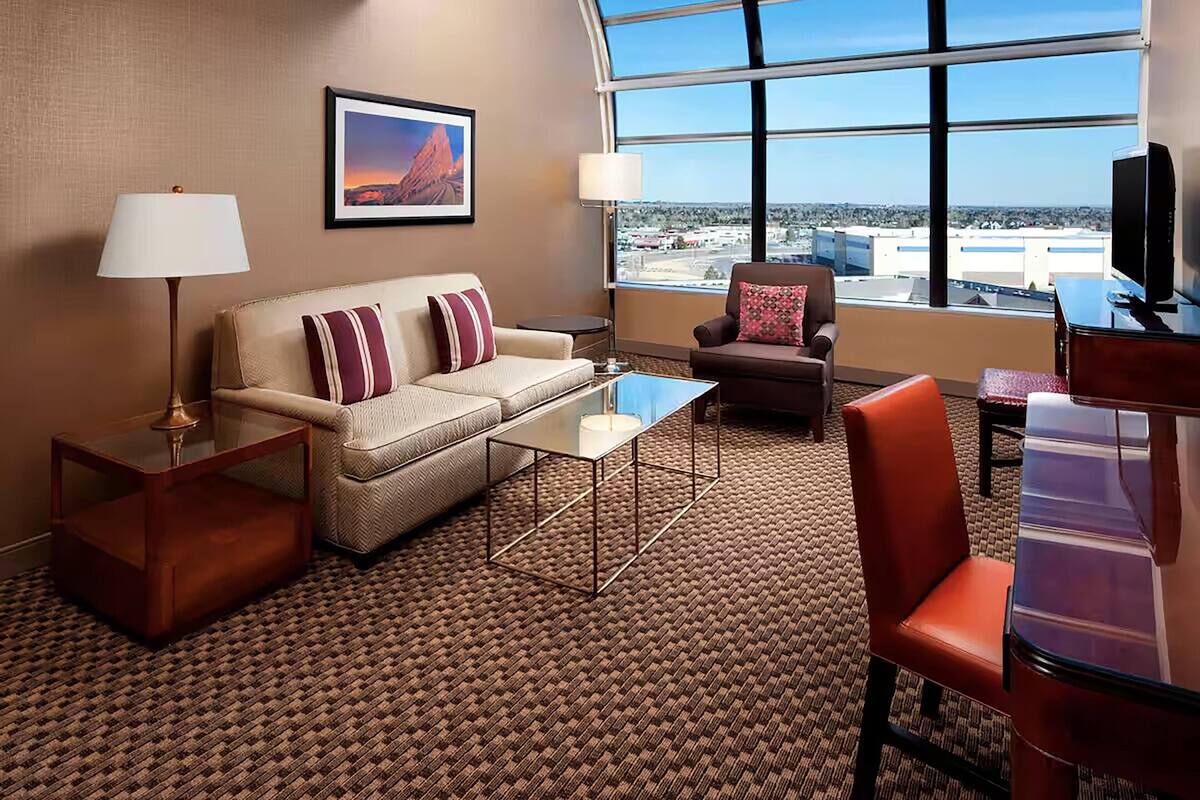 Hotelkamer met een bank, fauteuil, salontafel, televisie en een groot raam met uitzicht op de stad.