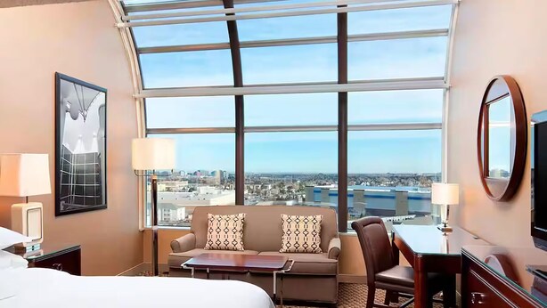 Une chambre d’hôtel avec une grande fenêtre, un lit, un canapé, un bureau et une chaise.