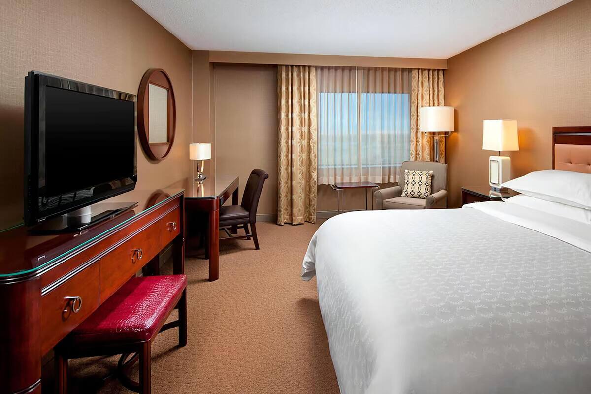 Une chambre d’hôtel avec un lit, un bureau avec une télévision, une chaise, une lampe et une fenêtre avec des rideaux.
