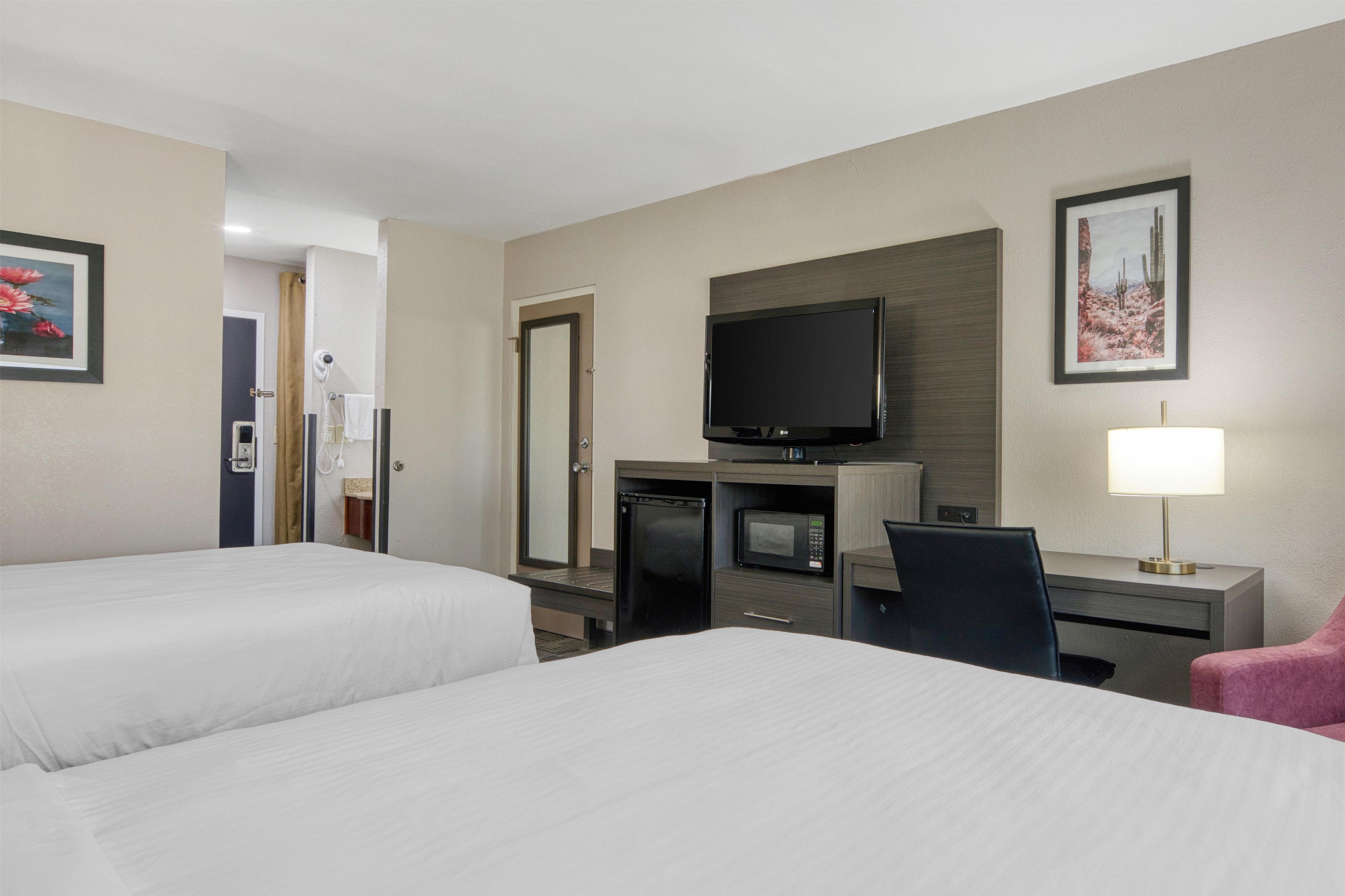 Una habitación de hotel con dos camas, televisión, escritorio con lámpara y microondas.