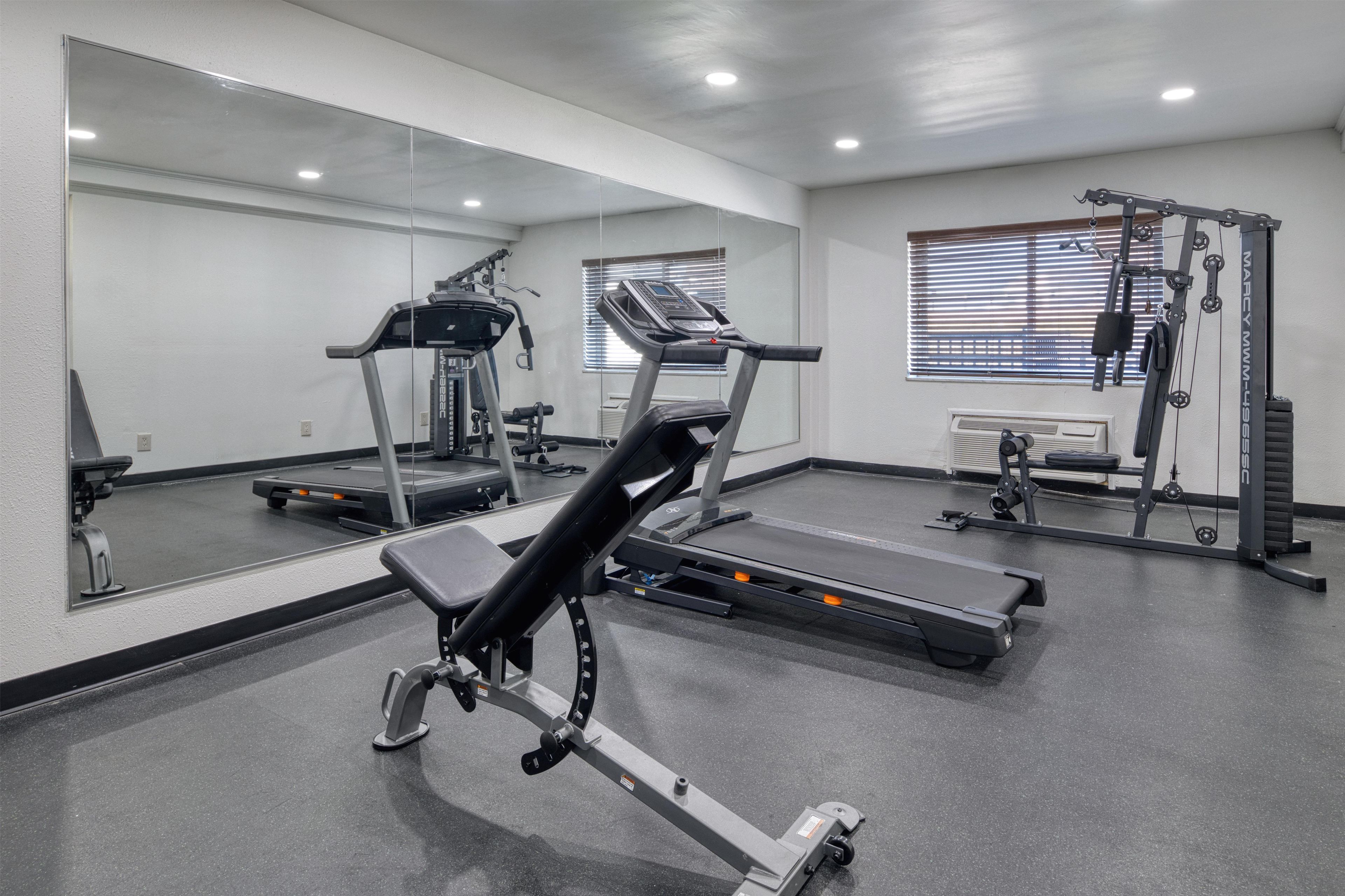 A gym with exercise equipment, including treadmills and weight machines, and a large mirror on the wall.