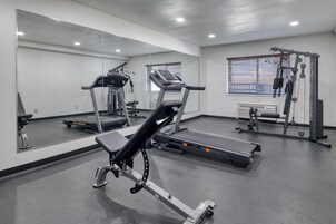 Un gimnasio con equipo de ejercicio, incluyendo cintas de correr y máquinas de pesas, y un espejo grande en la pared.