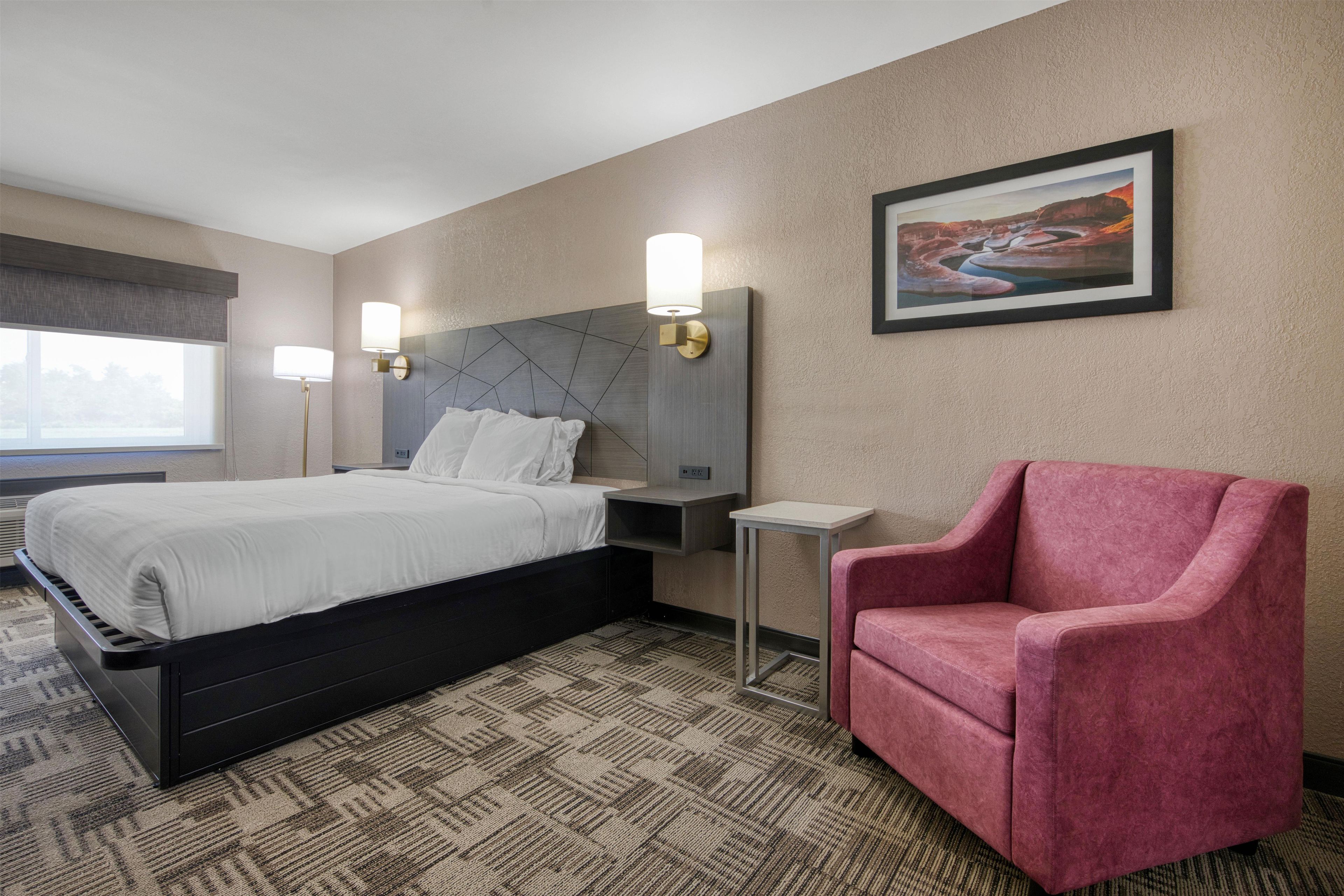 A hotel room with a bed, a chair, a nightstand, a lamp, and a painting on the wall.