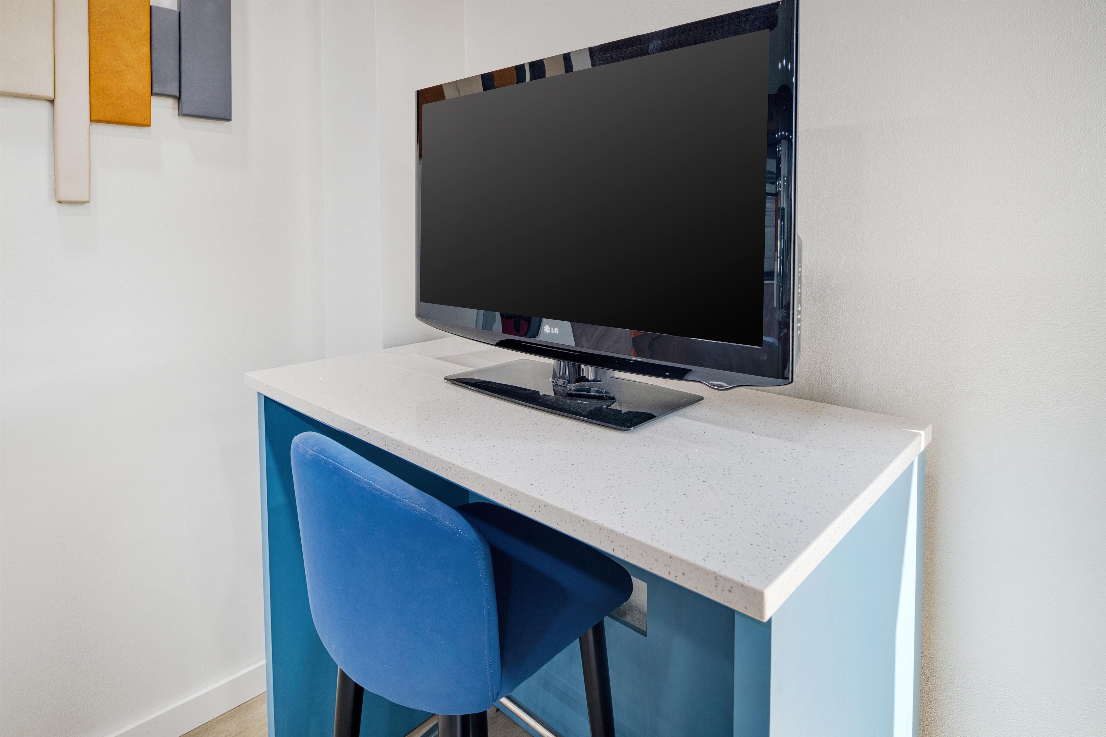 A modern office desk with a flat-screen monitor, keyboard, and a blue chair.