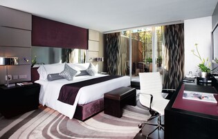 A modern hotel room with a large bed, a desk, and a view of the outdoors.