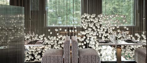 Um interior moderno com uma área de jantar que apresenta uma mesa de vidro, assentos acolchoados e um lustre decorativo.