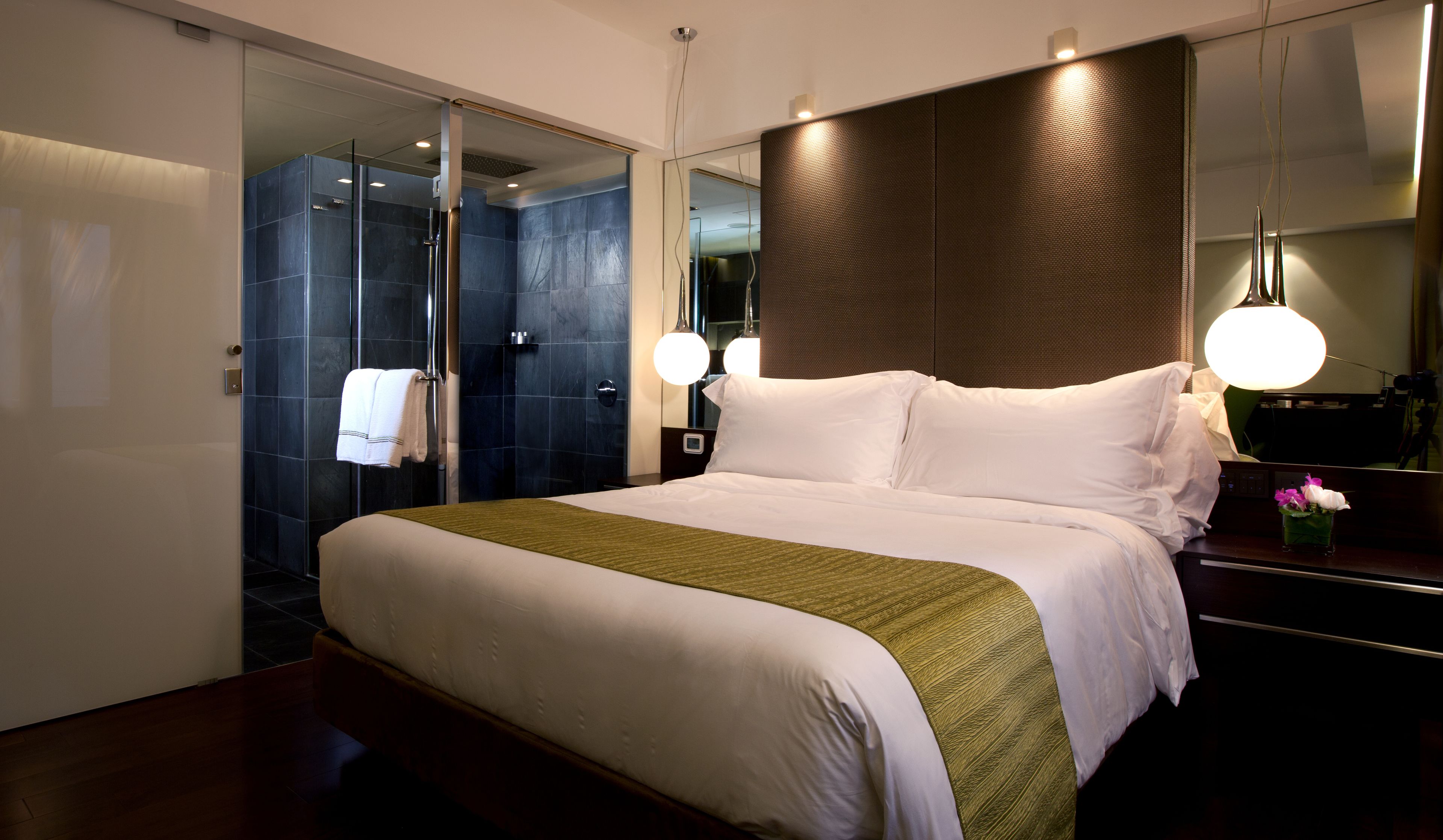 A modern hotel room with a large bed, a glass shower enclosure, and a large mirror.