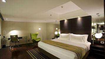 Una habitación de hotel moderna con una cama grande, un escritorio con una silla, una silla verde y un espejo.