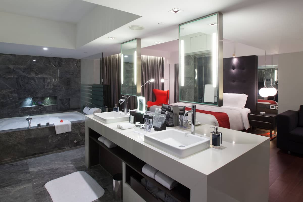 A modern bathroom with a large mirror, two sinks, a bathtub, and a shower.