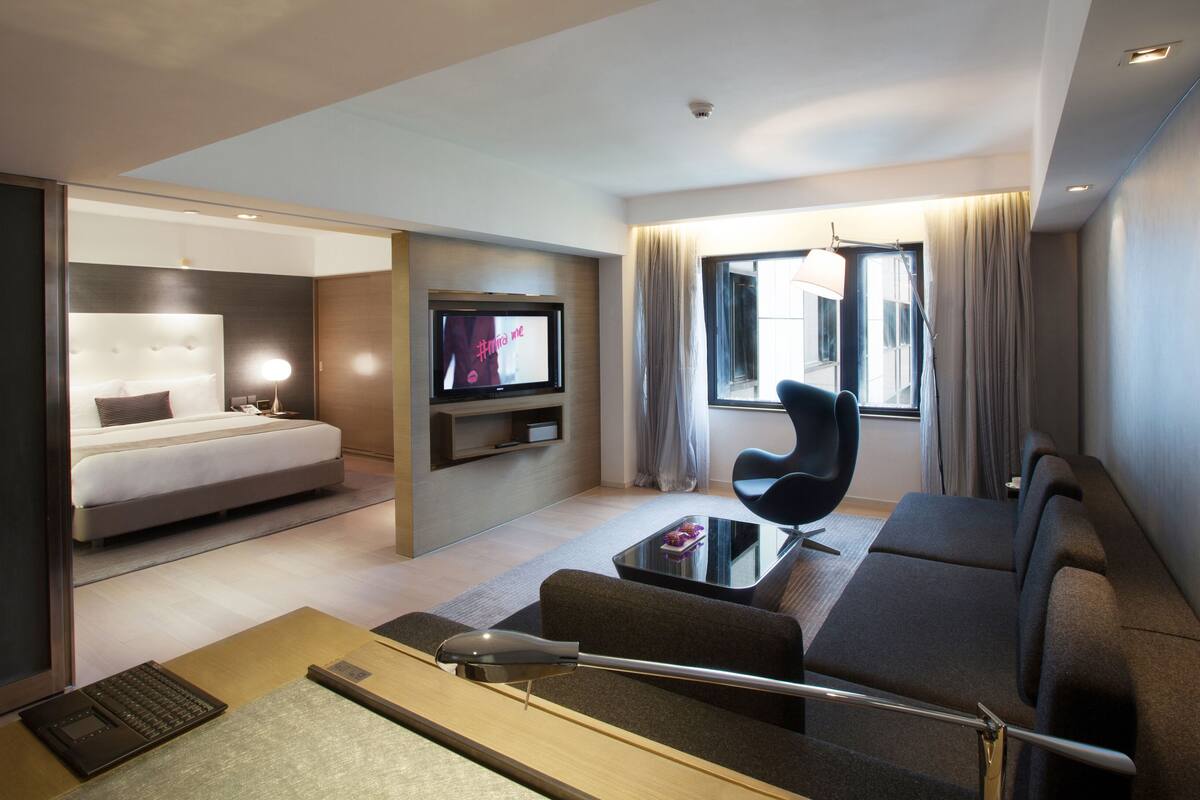 A modern hotel room with a bed, a TV, a sofa, and a desk with a laptop.
