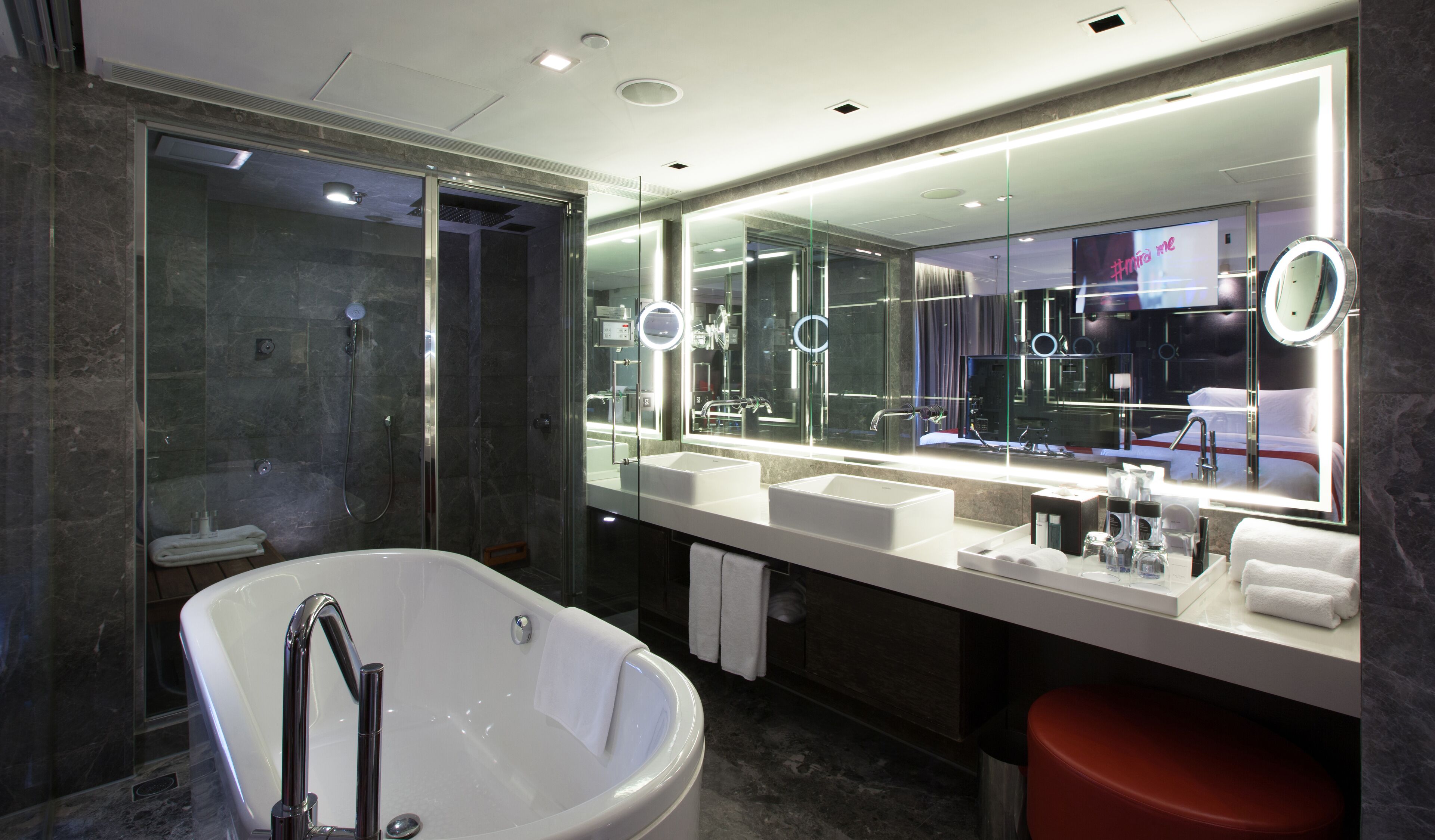 A modern bathroom with a freestanding bathtub, dual sinks, and a large mirror with integrated lighting.