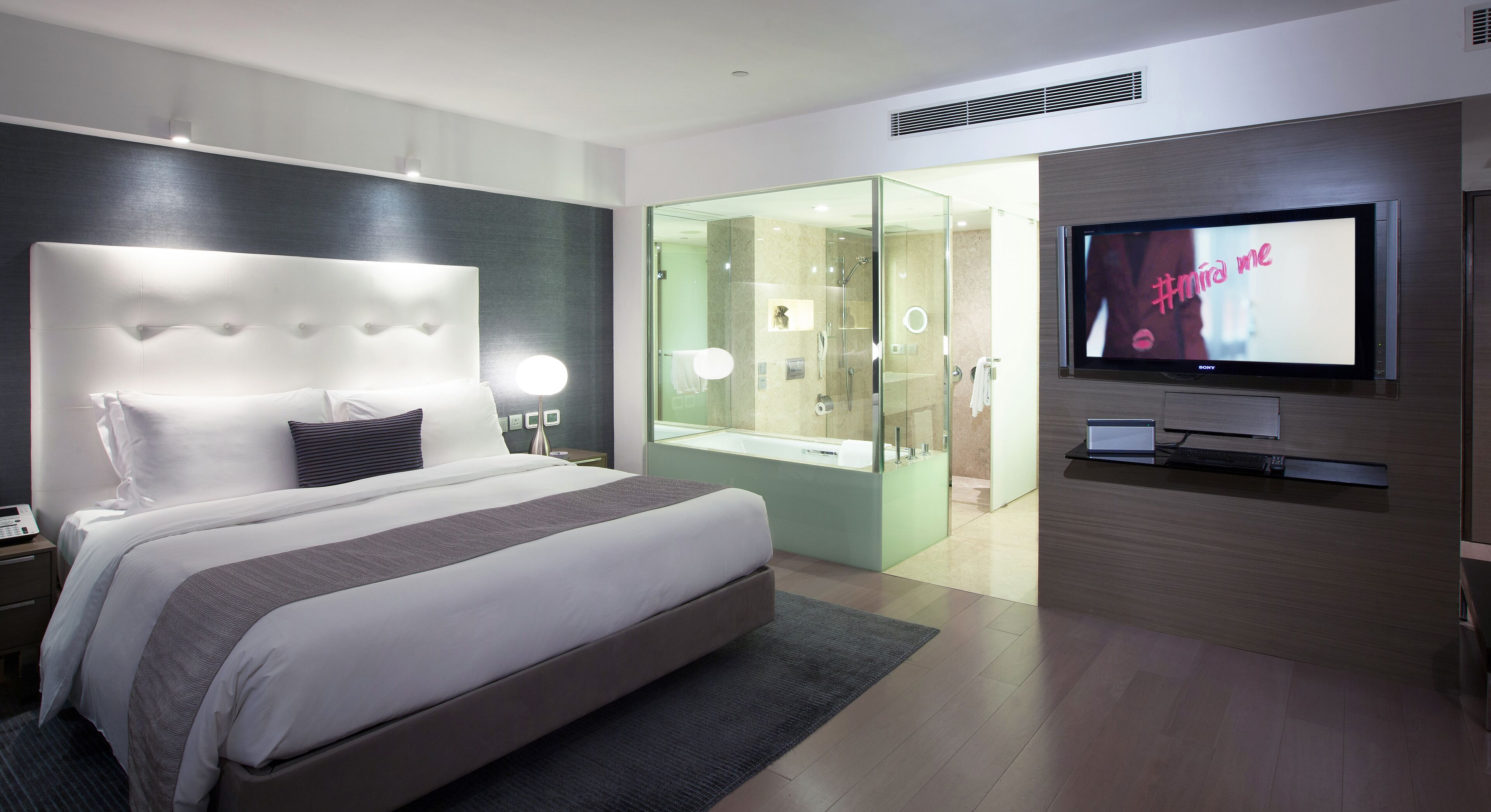 A modern hotel room with a large bed, a TV, and a glass-enclosed shower area.