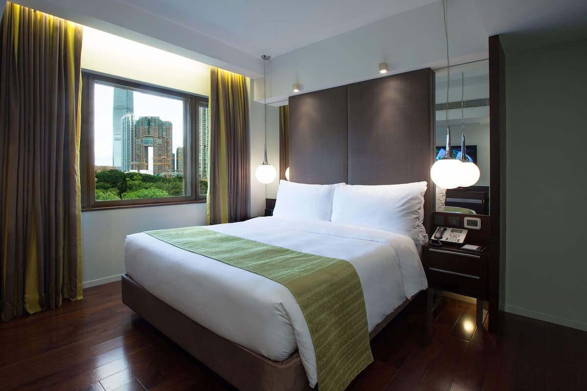 A hotel room with a large bed, a nightstand with a phone, a mirror, and a window with curtains.