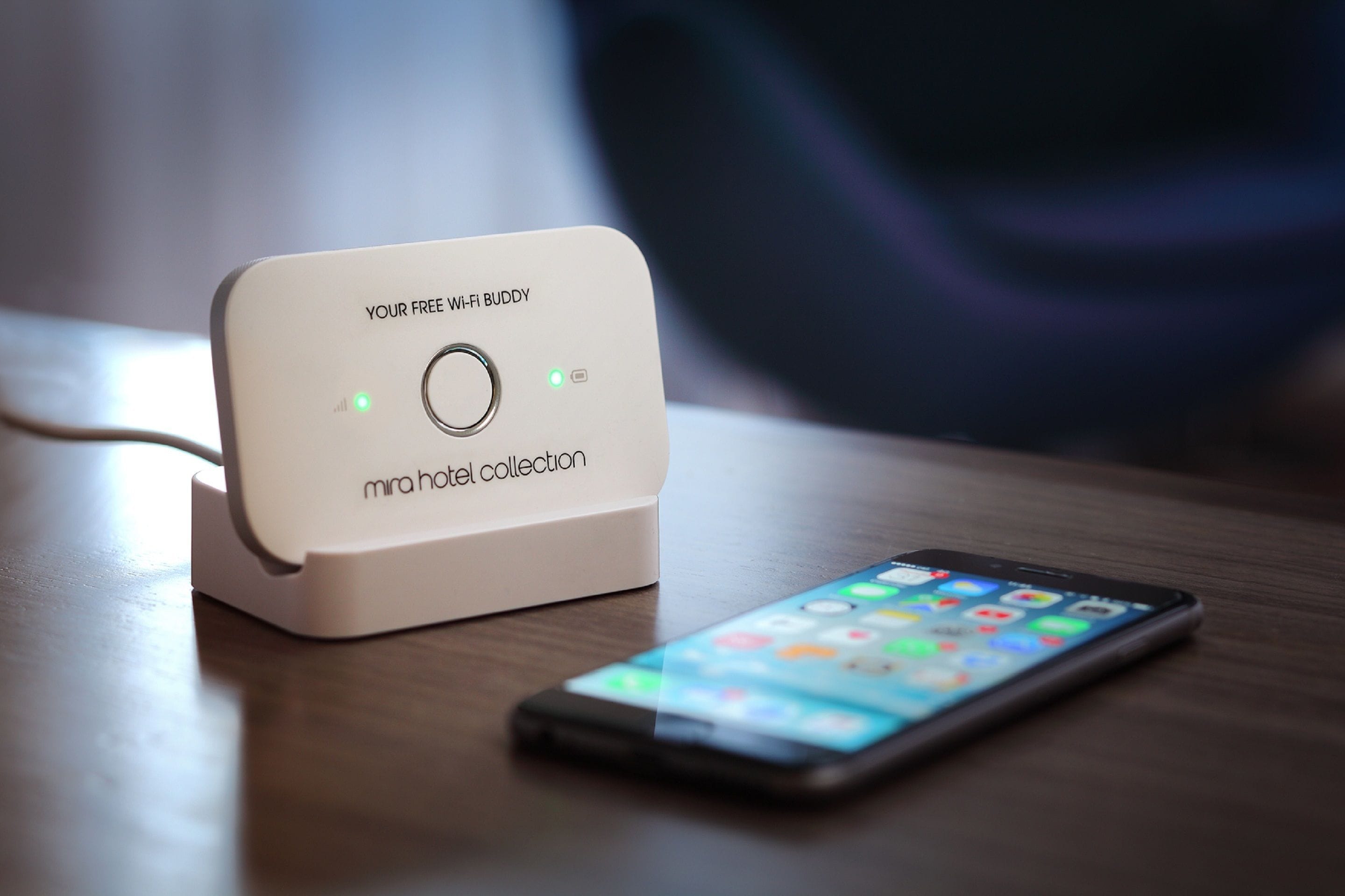 A Mira Hotel Collection charging station with a smartphone on a wooden surface.