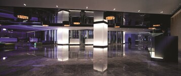 A modern lobby with a polished marble floor, a central light column, and a reception desk.
