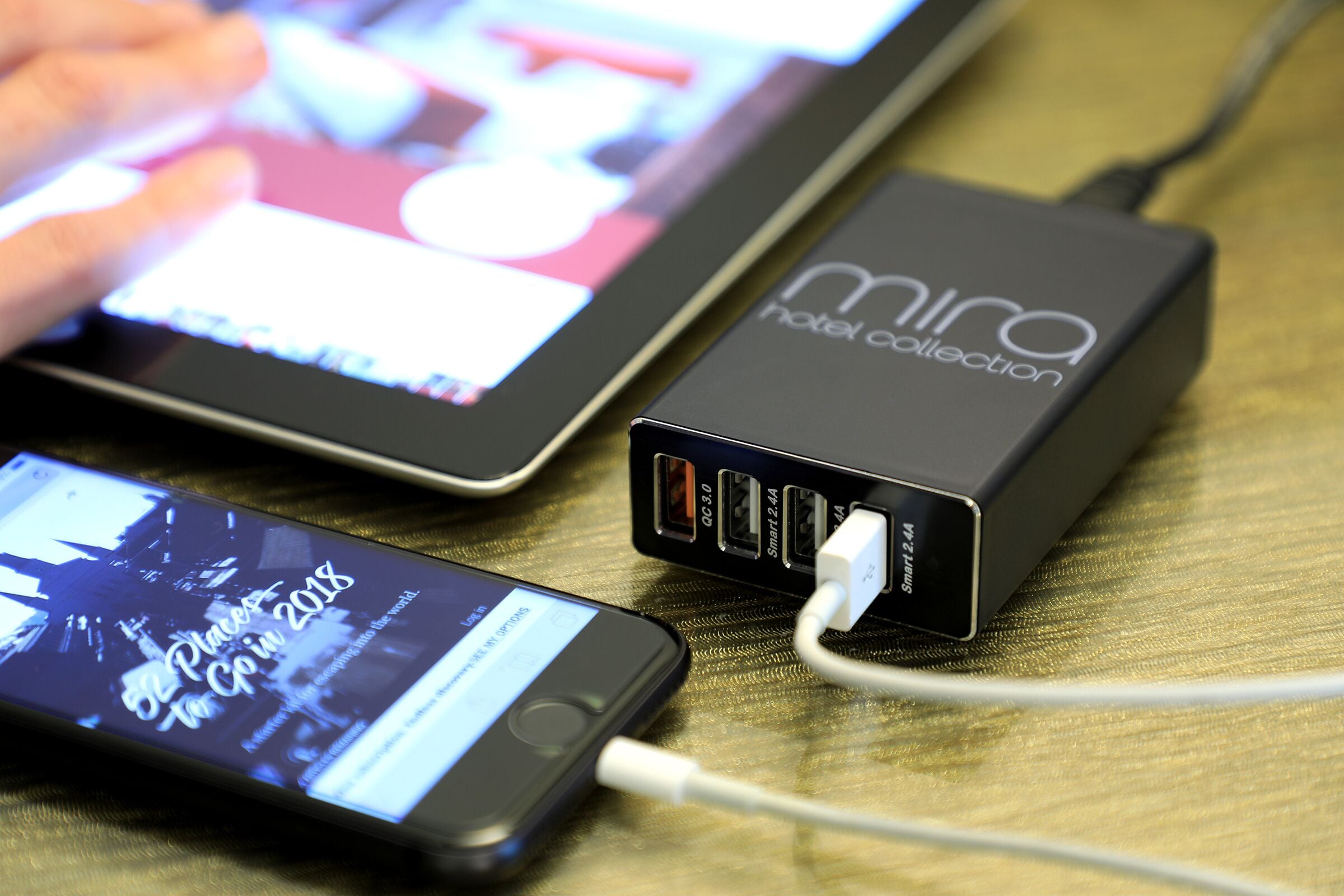 A smartphone connected to a power bank labeled "Mira Hotel Collection" with multiple USB ports.