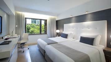 A hotel room with two beds, a desk with a computer, a chair, and a window with curtains.