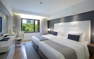 A hotel room with two beds, a desk with a computer, a chair, and a window with curtains.