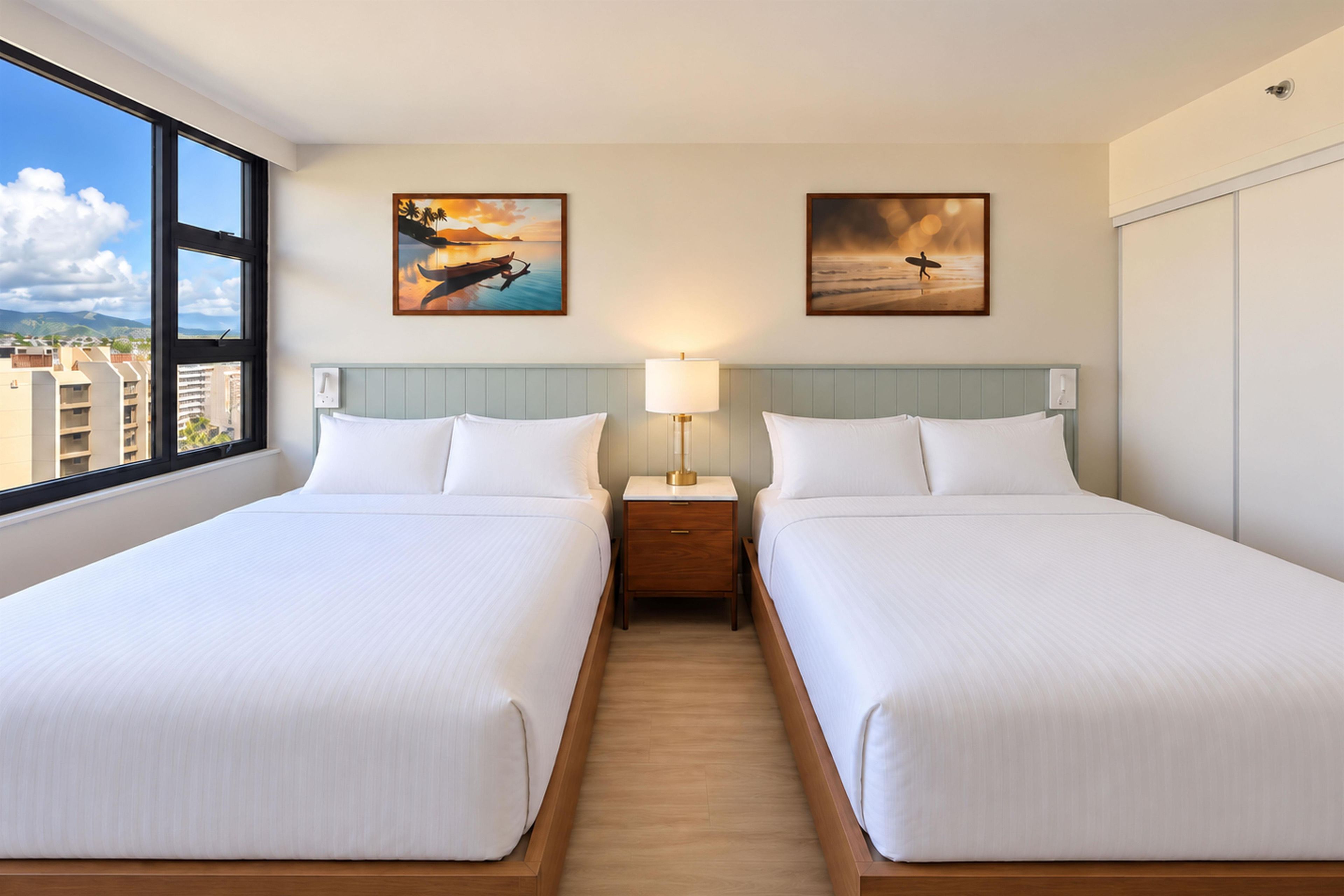 A hotel room with two beds, a nightstand with a lamp, and two paintings on the wall.
