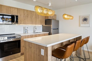 A modern kitchen with wooden cabinets, stainless steel appliances, a white countertop, and two pendant lights. - Aston at the Waikiki Banyan (Honolulu)