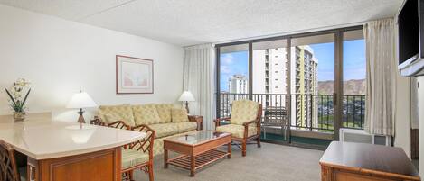 A hotel room with a sofa, armchair, coffee table, and a TV.
