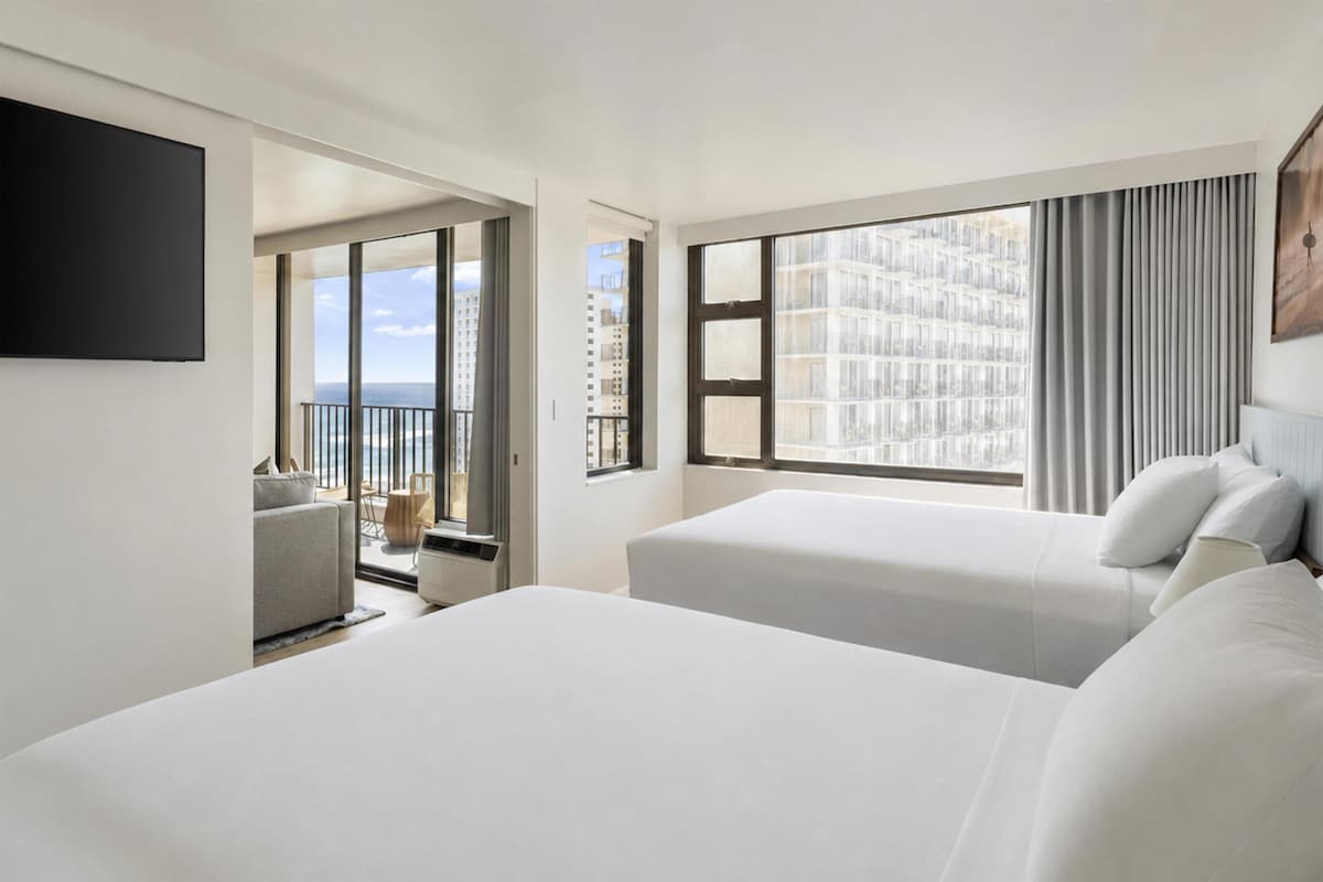 A hotel room with two beds, a balcony, and a city view.