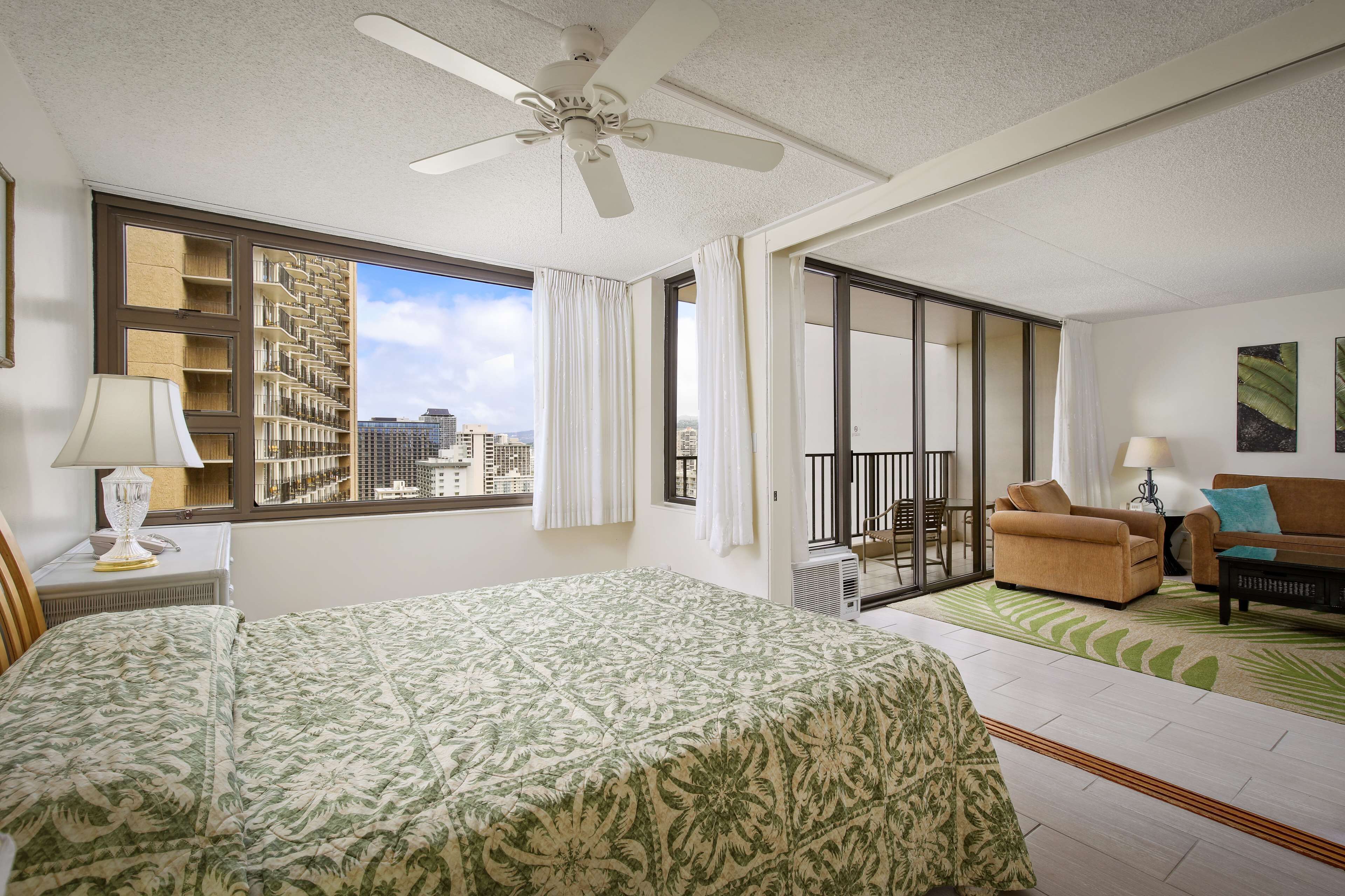 A hotel room with a bed, a sofa, a balcony, and a city view.