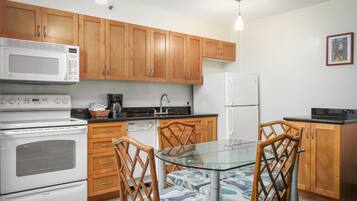 Une cuisine avec des meubles de rangement en bois, un four à micro-ondes, une cuisinière, un réfrigérateur et une table en verre avec des chaises.