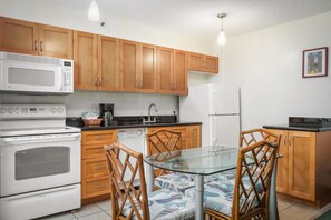Una cocina con armarios de madera, microondas, estufa, refrigerador y una mesa de vidrio con sillas.